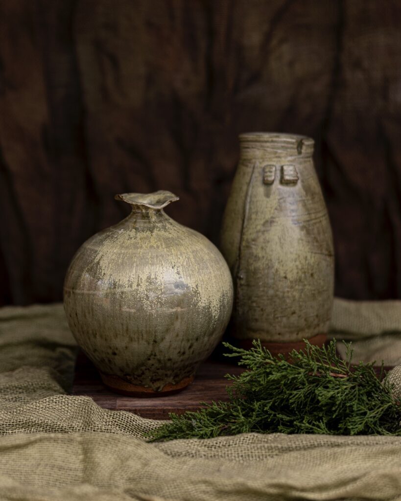 Two ceramic pottery vases that have an old look to them. One is bulbous while the other is a taller vase.