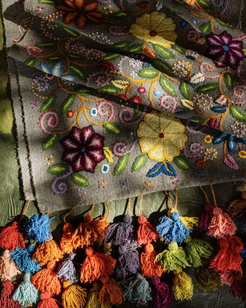 A handmade woven blanket with colorful tassels and embroidered flowers.