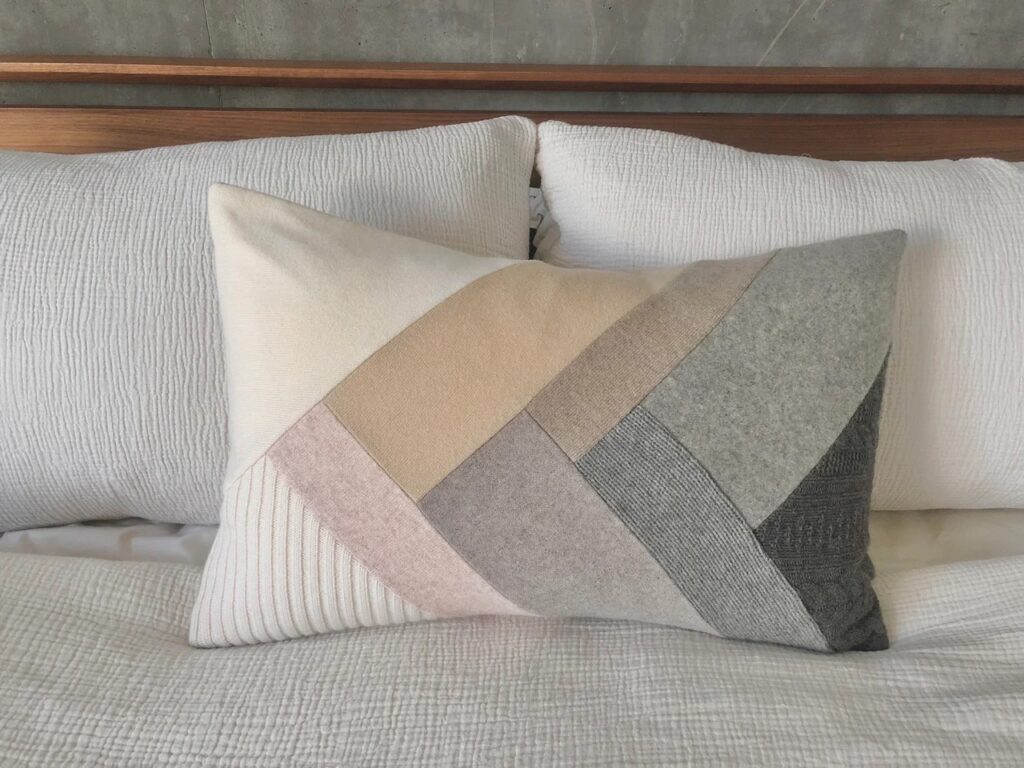 Three pillow sit on a bed. The back two are white pillows while the one in front has an arrow pattern in brown, grey, and black.