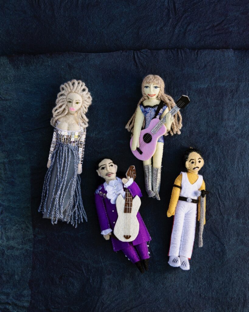 Four ornaments sit on a black background and are made of felt to look like Dolly Parton, Prince, Taylor Swift, and Freddie Mercury.