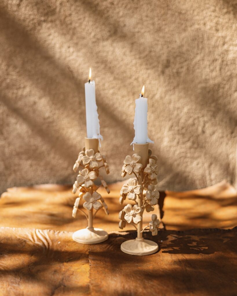 Two candlesticks for the home with lit candles sit on an ochre background.