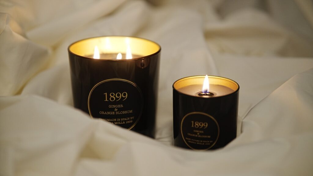 Two black candles that say "1899" sit lit on a whtie sheet.