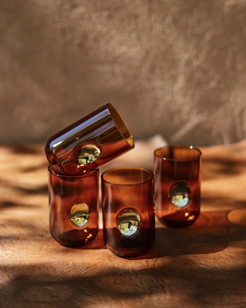 A four glass set in dark beer bottle brown sit on an ochre background.