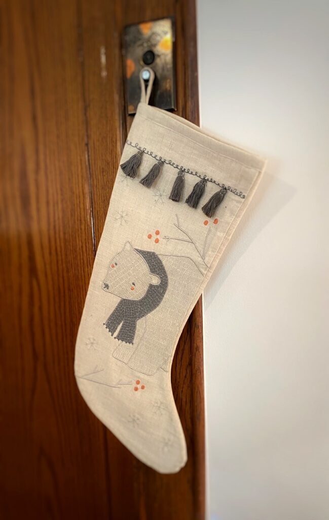 A white stocking with a polar bear and tassels hands from a holder on a wood wall. 