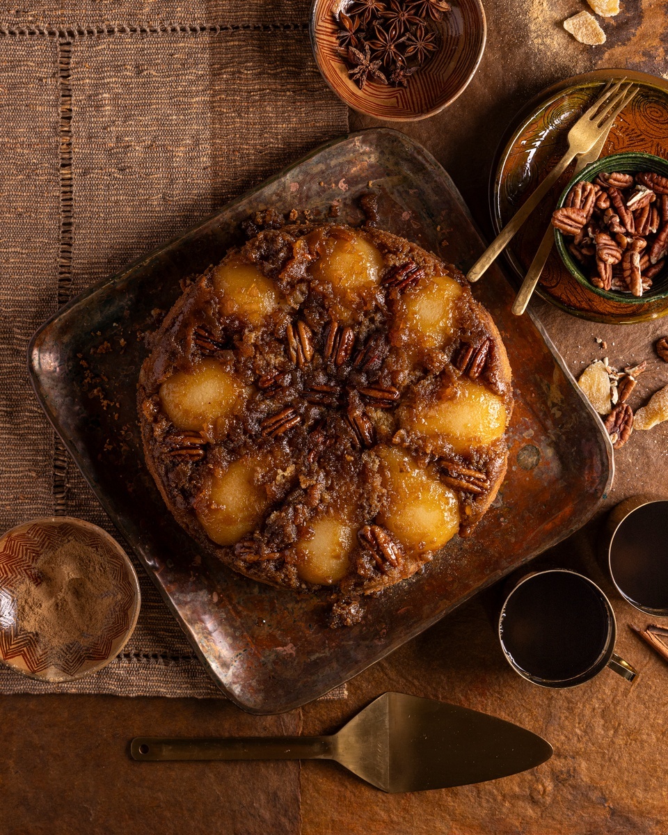 A ginger pear upside-down cake served on a wooden board surrounded by fresh rosemary.