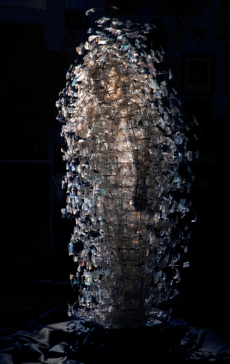 Abstract glass sculpture composed of numerous shattered pieces coming together to form a towering illuminated structure evoking themes of reconstruction and artistic innovation.