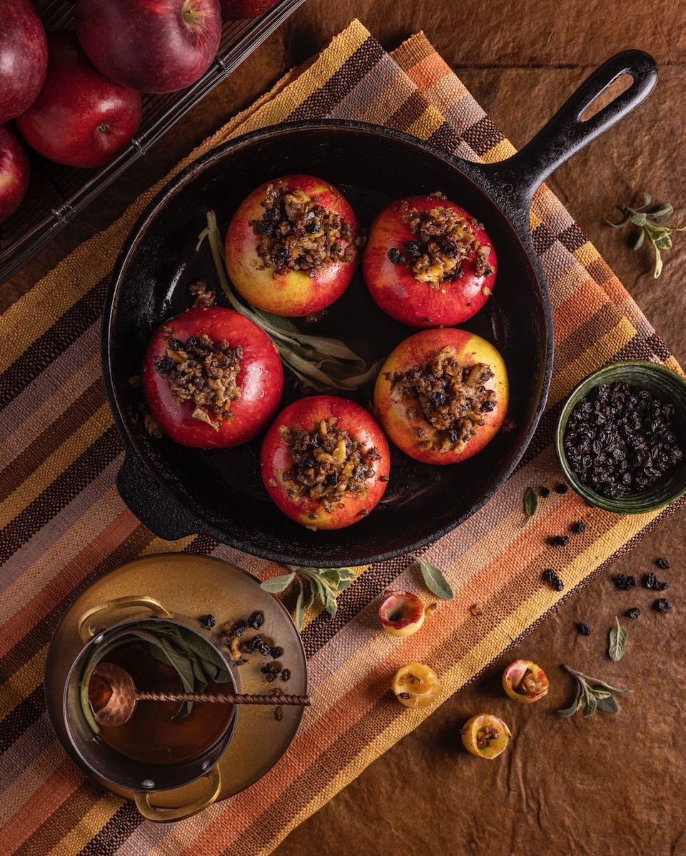 Four baked apples stuffed with sausage plated rustically on a wood background