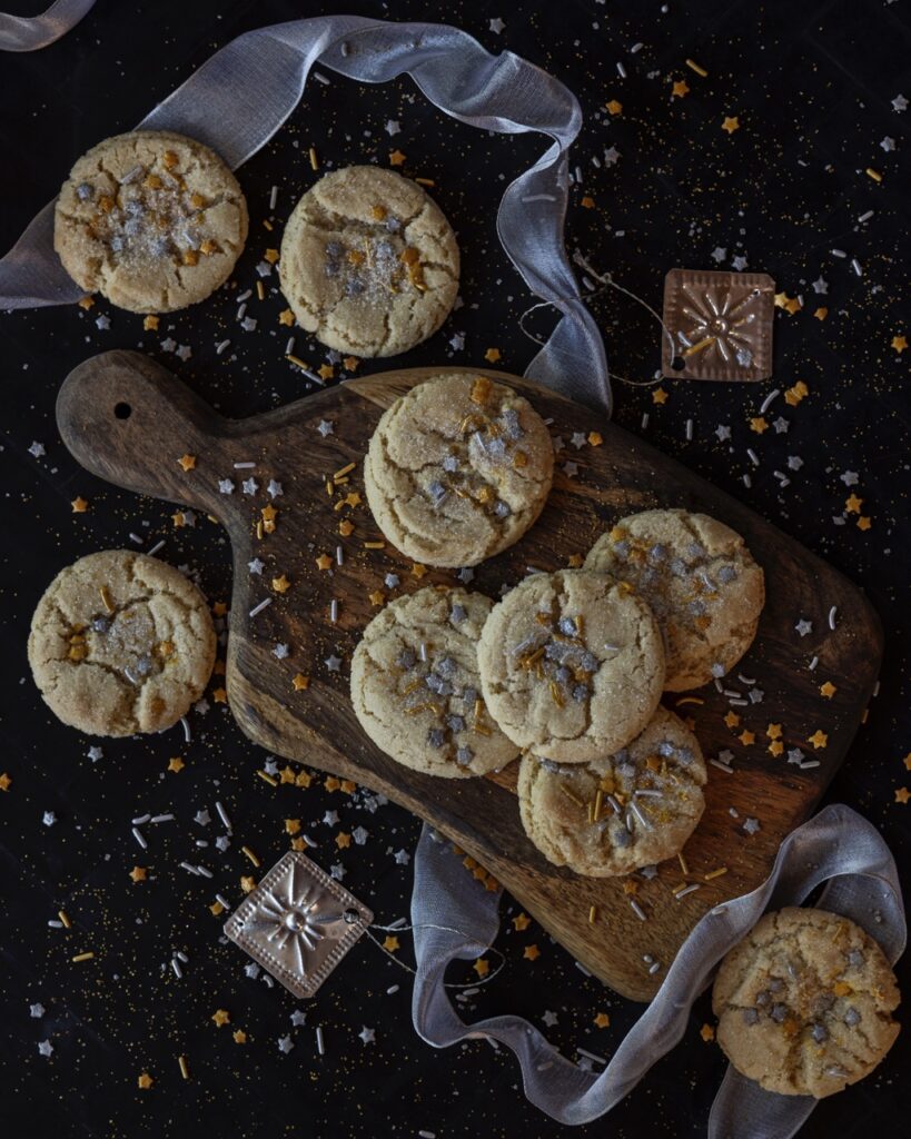 A group of Crackly Sugar Cookies sit on a brown sitting board with festive decorations around them.