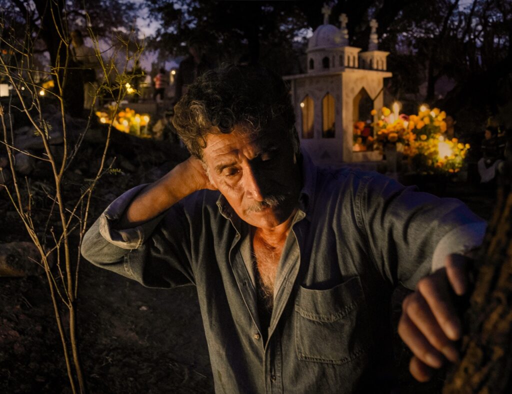 A man leans with his hand on his face with candles burning in the background.