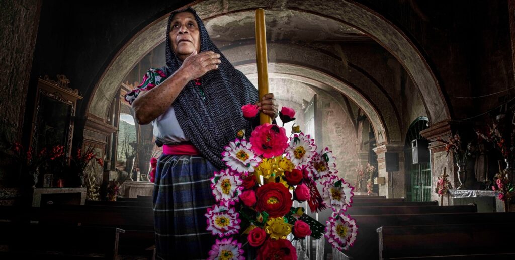 A woman covers her hand across her heart behind an ofrenda.