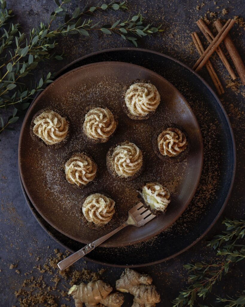 On a brown plate sits little cookie cups with a swirl of icing and cinnamon on top of them.