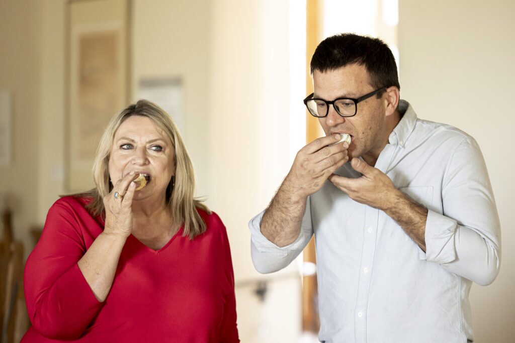 A woman in a red shirt and man in a blue shirt bite into Holiday cookies.