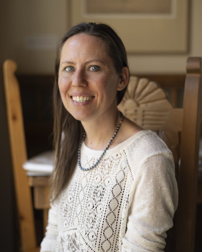 A woman baker in a white sweater sits in a chair for a portrait.