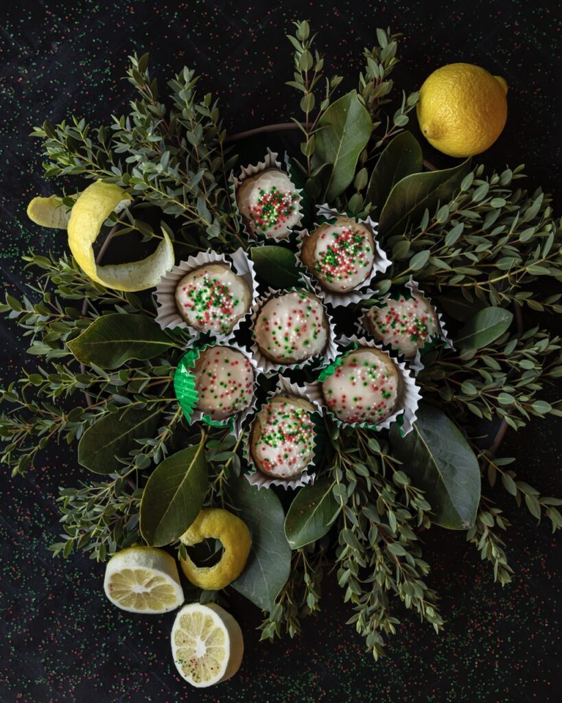 A small pile of Lemon Ricotta Cookies sit on leaves of greenery with lemon peels scattered throughout.