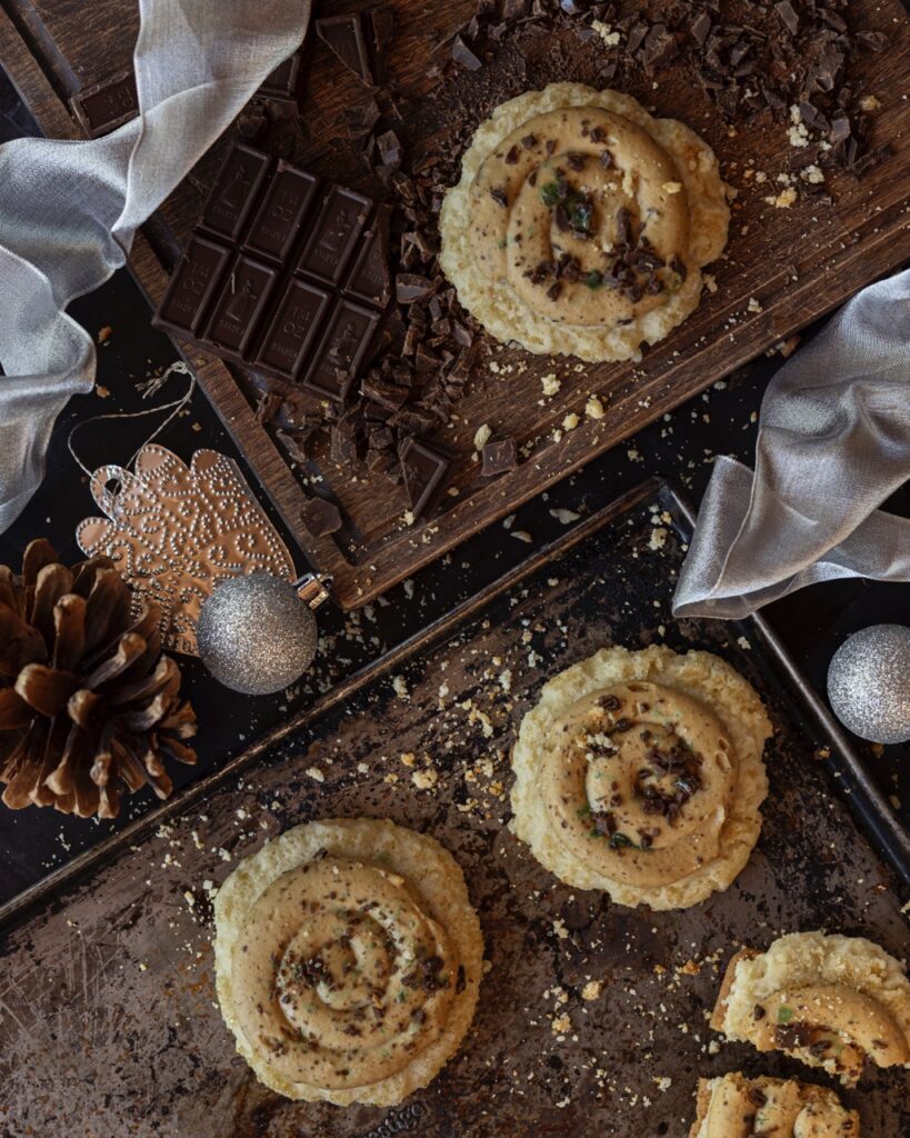 Two baking trays hold a few brownish sugar cookies with peppermint topping.