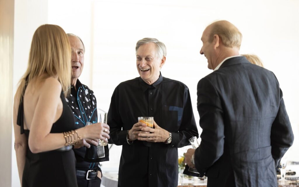 Four people (three men and a woman) speak in a group while holding cocktails in their hands.