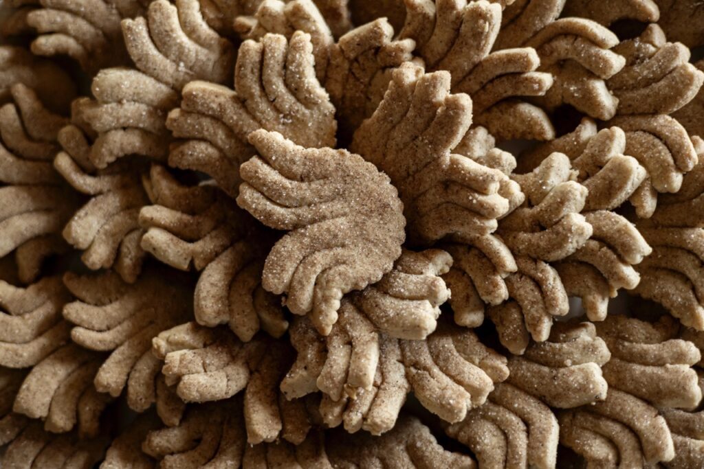 A big pile of biscochitos in yucca flower shapes with a dusting of cinnamon sugar and chai spice on top. 