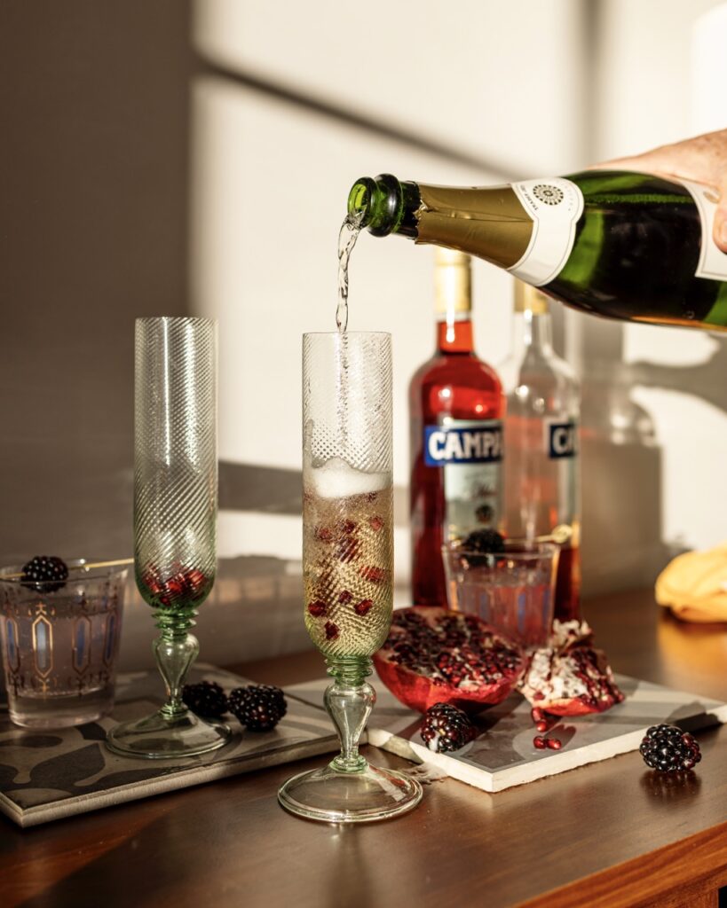 A person pours prosecco into a Pomegranate cocktail.