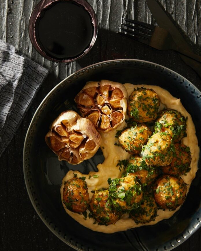 Herb Crusted Chicken Meatballs with Smoked Garlic Aioli in a pan on the side of a fork, a napkin, and a drink
