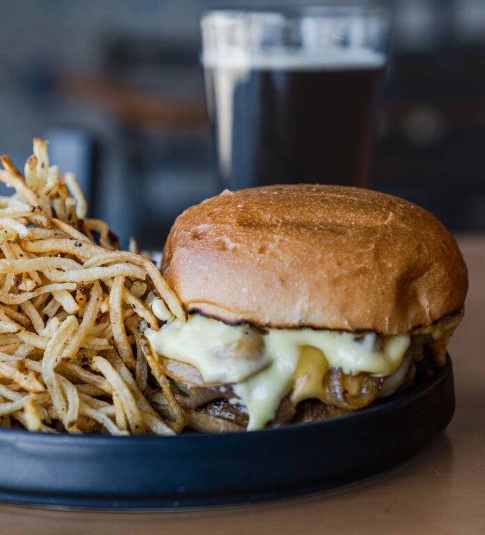 Mesa Provisions' Mesa Burger sits on a round black plate with string fries to the left of the burger.