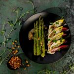 Grilled asparagus with green chile ricotta sits on a black plate.