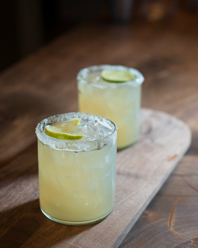 Two glasses with a pale yellow margarita with lime slices floating on top.
