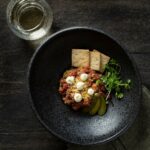 Aerial view of Prime Steak Tartare on a small, black, bowl looking plate.