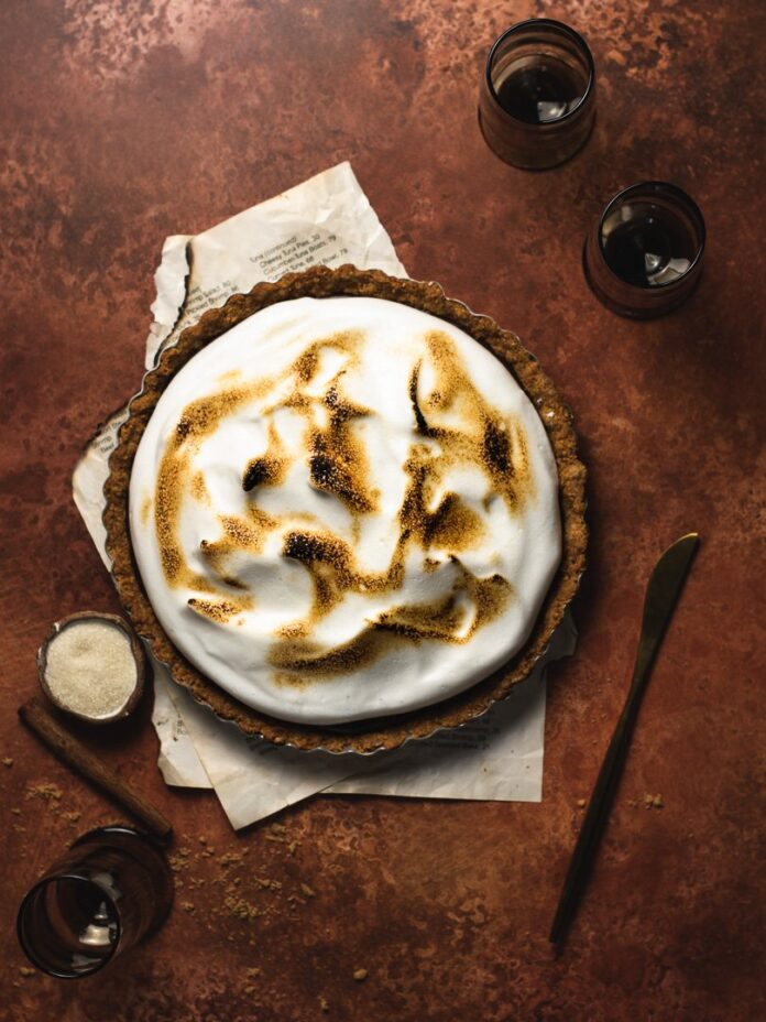 Vegan Mexican Chocolate Tart served on a brown plate, which is placed on two partially-burnt papers Three small glasses, a knife, and a small bowl of sugar on the sides