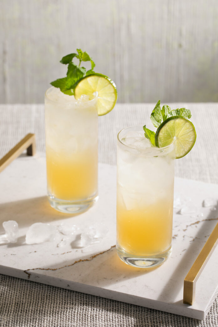Two mojito cocktails, clear on top and yellow on the bottom, in highball glasses and garnished with lime wedges and mint. Mojito Recipe