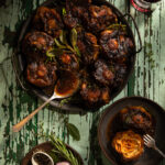 Flat-lay image of Green Chile Braised Oxtail in a cast-iron pan set on a weathered table. Braised Oxtail Recipe