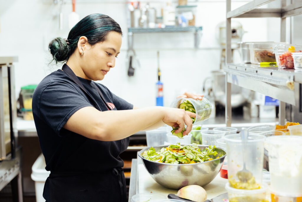 A kitchen staff member prepares a salad at the kitchen station.