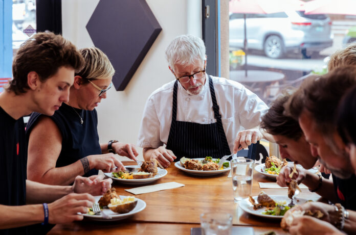 The staff of Horno restaurant enjoy a fried chicken meal at a table in the restaurant with the owner.