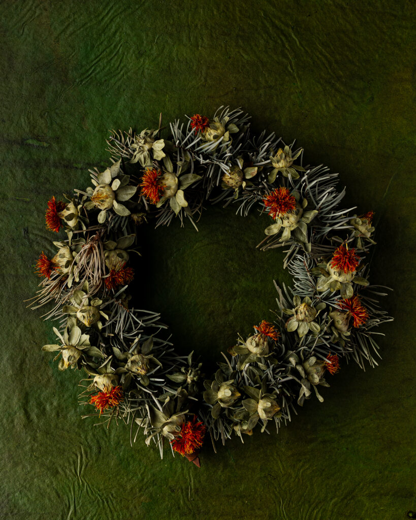 A wreath made of dried and fresh flowers, red and green in color.