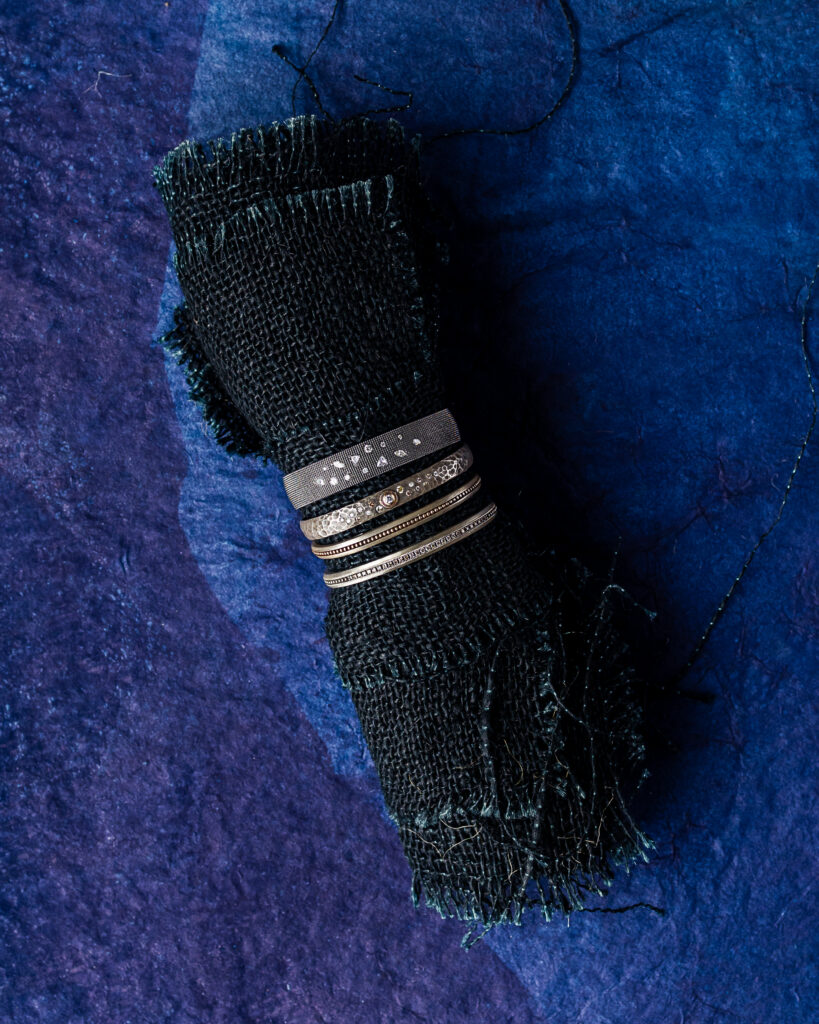 four thin, silver cuffs on a rolled up black cloth. the top two have diamonds. jewelry gifts for women