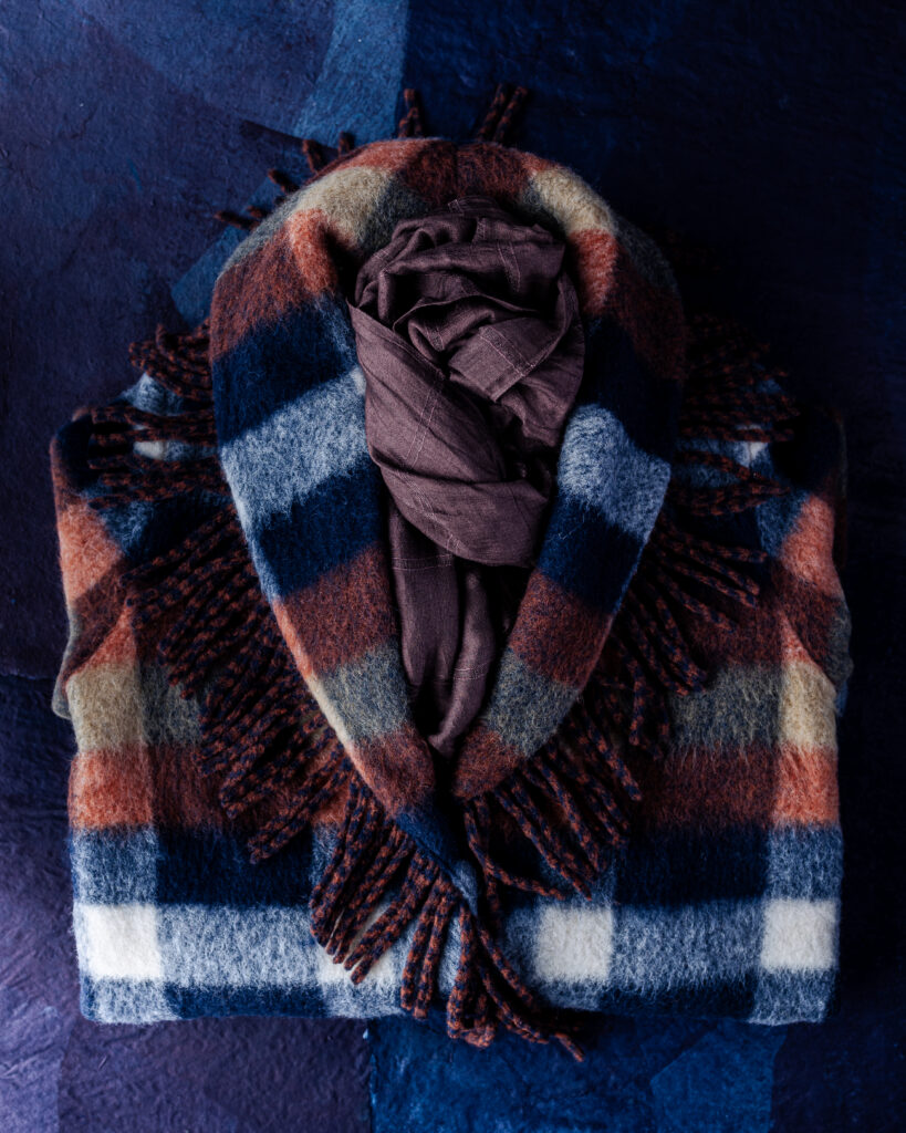A classic plaid, soft wool-blend coat in sapphire blue, rust, white and beige that hits just above the knee. A fringe-lined shawl collar and front patch pockets.