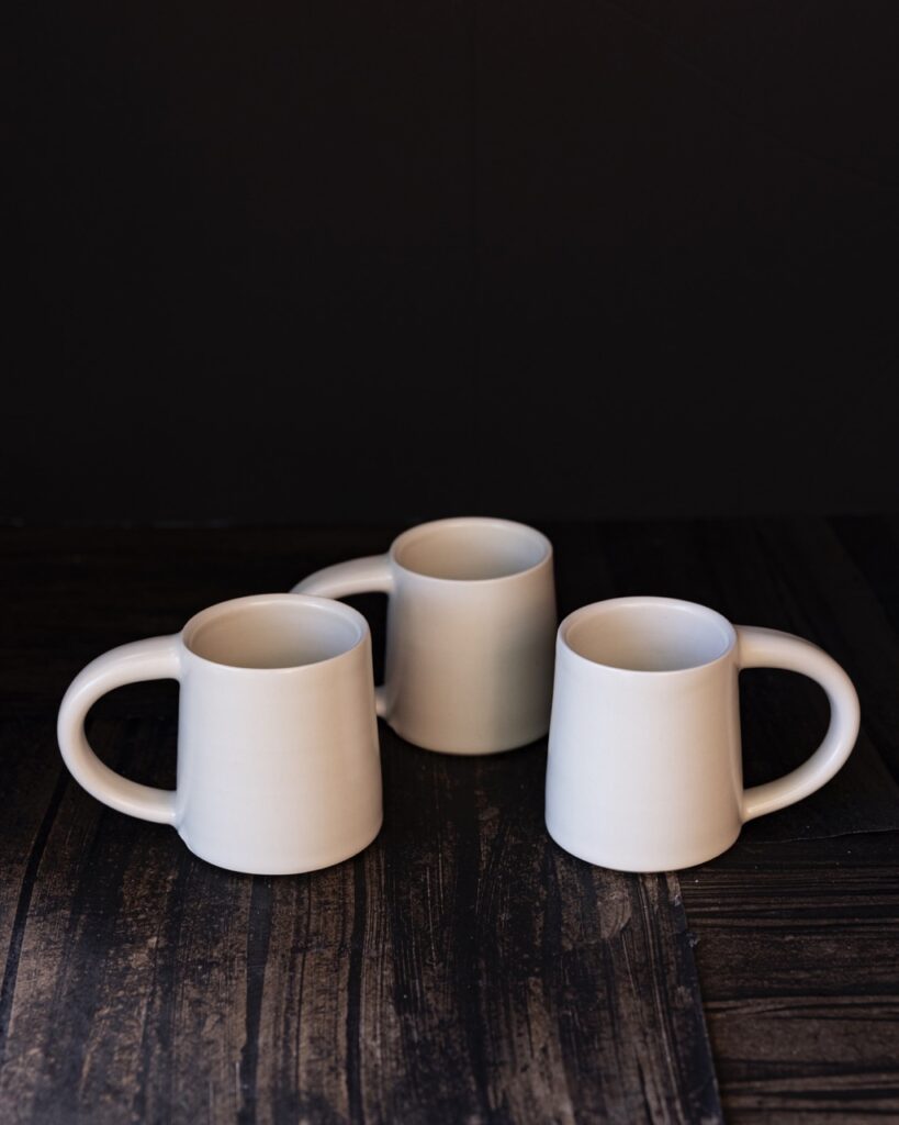 Three while handmade coffee cups sit on a black textured background.