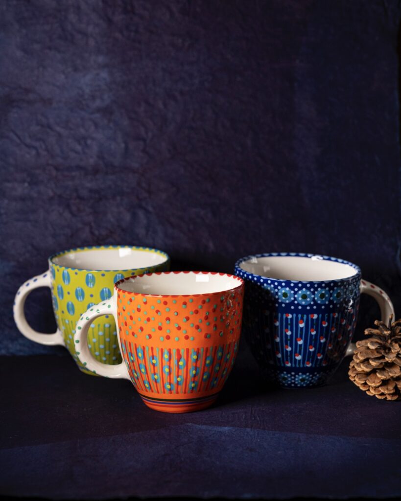 Three cups sit ona. blue background in green, orange, and blue with dots all over each.