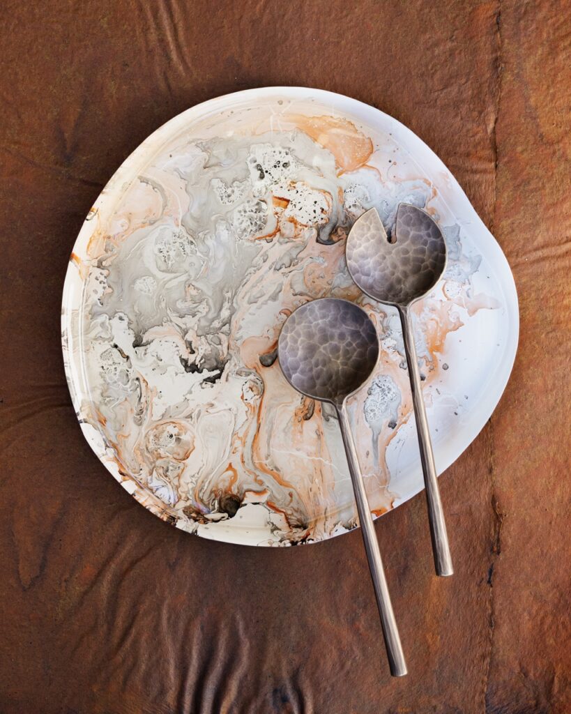 Two round circular spoons, one with a slice taken out of the head sit on an orange and grey marble plate, all on a brown table.