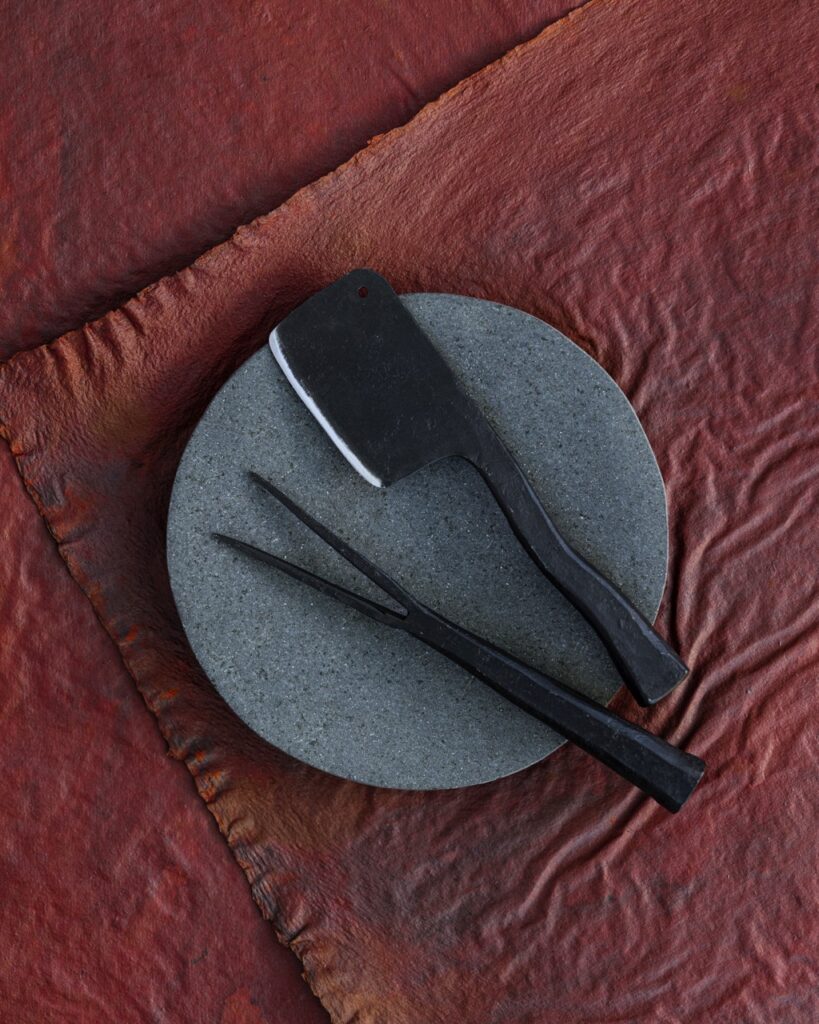 On a grey circular platform sits a vintage cheese knife and fork all on a red background.