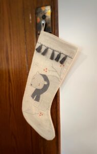 A white stocking with a polar bear and tassels hands from a holder on a wood wall.