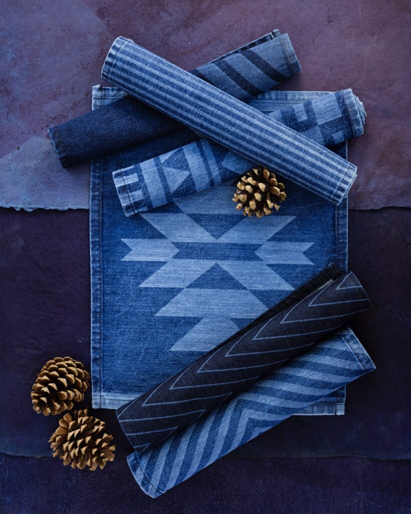 Various blue patterned placemats sit rolled up on a purple background with one placemat open under the rest.