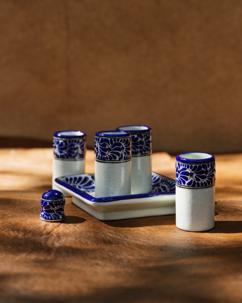 A ceramic glass and tray set for men in the colors blue and white sit on a brown background with sunlight peaking through.