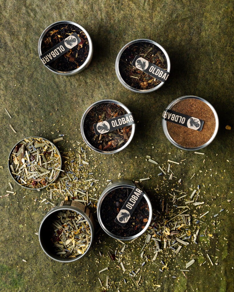 An aerial view of six open tins of loose leaf tea on a green table