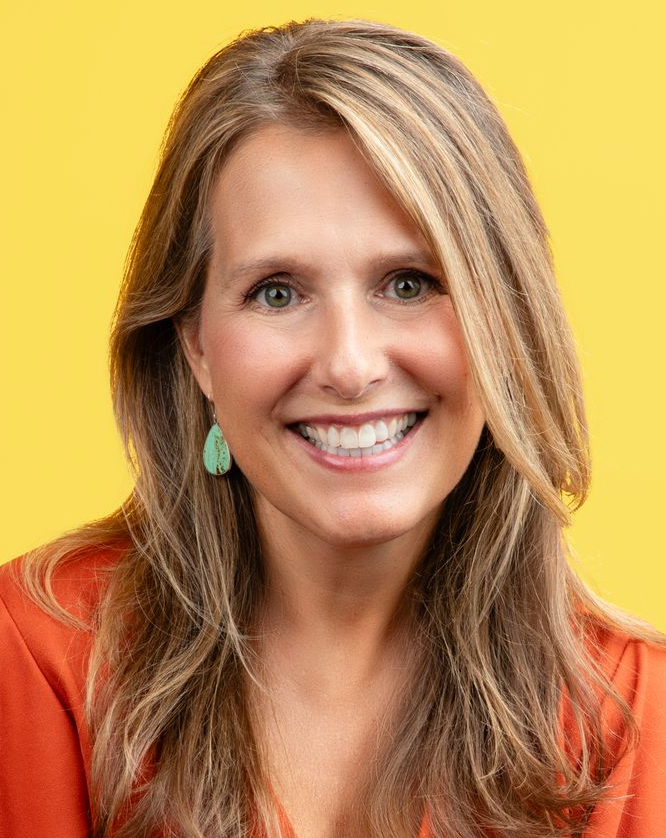 A photo of Stacey Edgar a woman, in front of a yellow background wearing an orange shirt, blue earrings, and a smile on her face.
