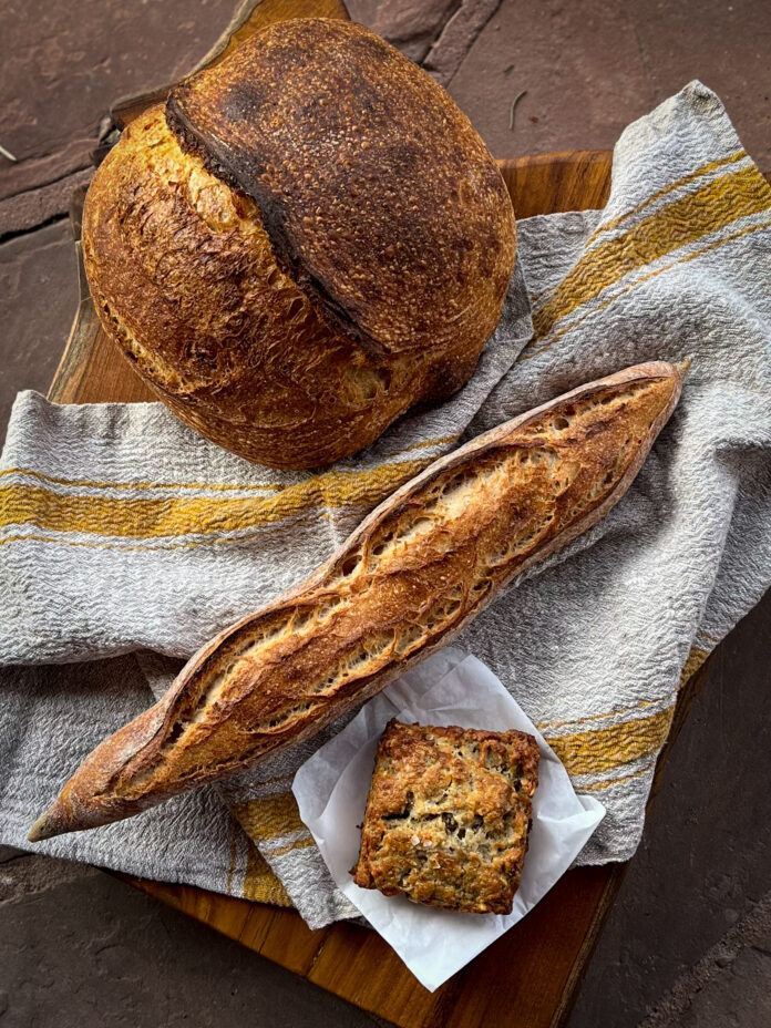 A loaf of sourdough bread sits next to a baguette and muffin on top of a towel as products from Bread Shop in Santa Fe.