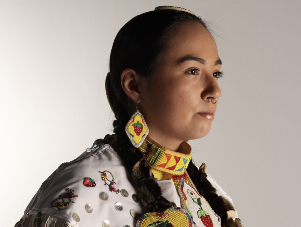 A woman's side profile is turned towards the camera with her hair in braids, strawberry bead earrings, and a beaded collar as well.