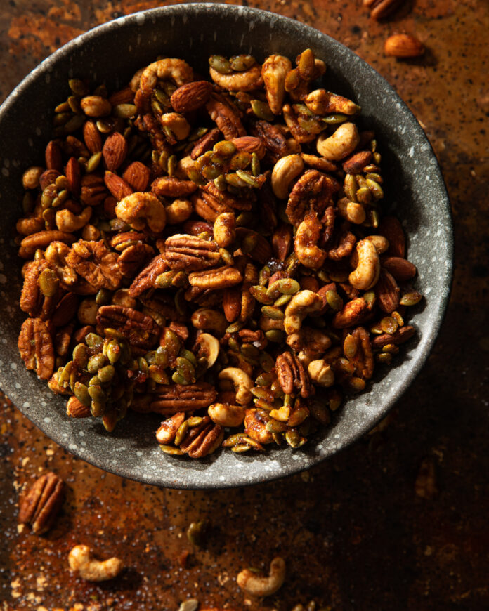 A light greyish blue bowl of seasoned variety nuts and pumpkin seeds on a wooden table