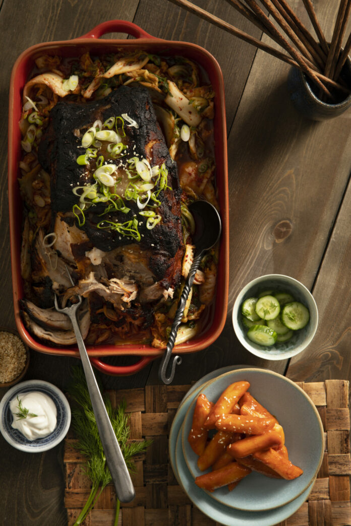 A tantalizinbraised pork shoulder & kimchi soup featuring Korean flavors, garnished with fresh dill, sour cream, scallions, and toasted sesame seeds.