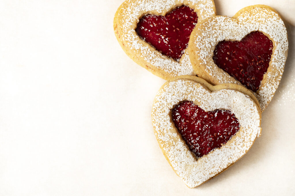 Three heat shaped cookies filled with jam and topped with powdered sugar sit to the right of a white background.
