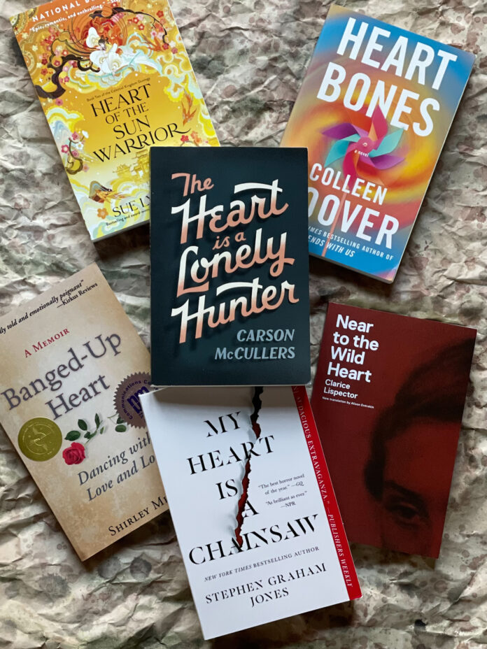 Six books sit stacked on top of a textured blanket with five books on the bottom and one sitting atop the rest.